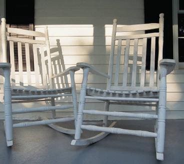 A group of white rocking chairs sitting on top of a porch.